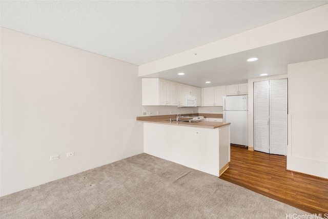 kitchen with kitchen peninsula, white appliances, sink, hardwood / wood-style flooring, and white cabinets