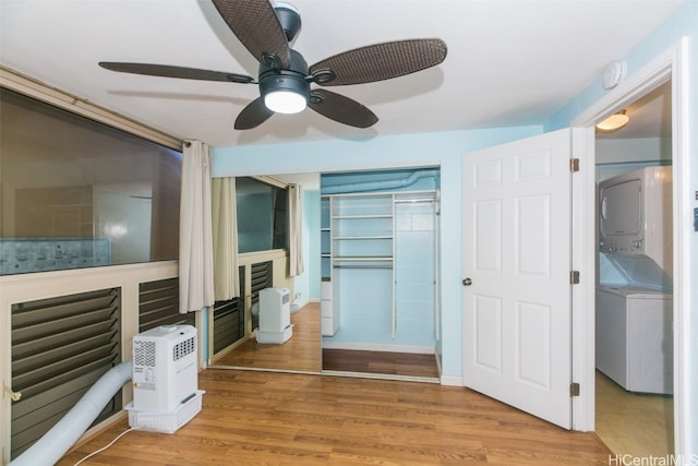 unfurnished bedroom featuring a closet, stacked washer / drying machine, light wood-type flooring, and ceiling fan