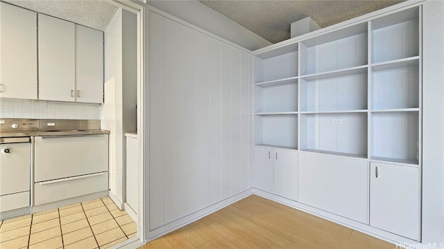 interior space featuring white cabinetry, light hardwood / wood-style floors, a textured ceiling, and backsplash