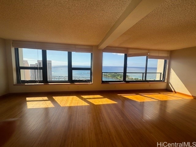 interior space featuring beam ceiling, a textured ceiling, a water view, and light wood-type flooring