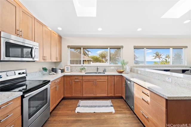 kitchen with light stone counters, appliances with stainless steel finishes, dark wood-type flooring, a skylight, and sink