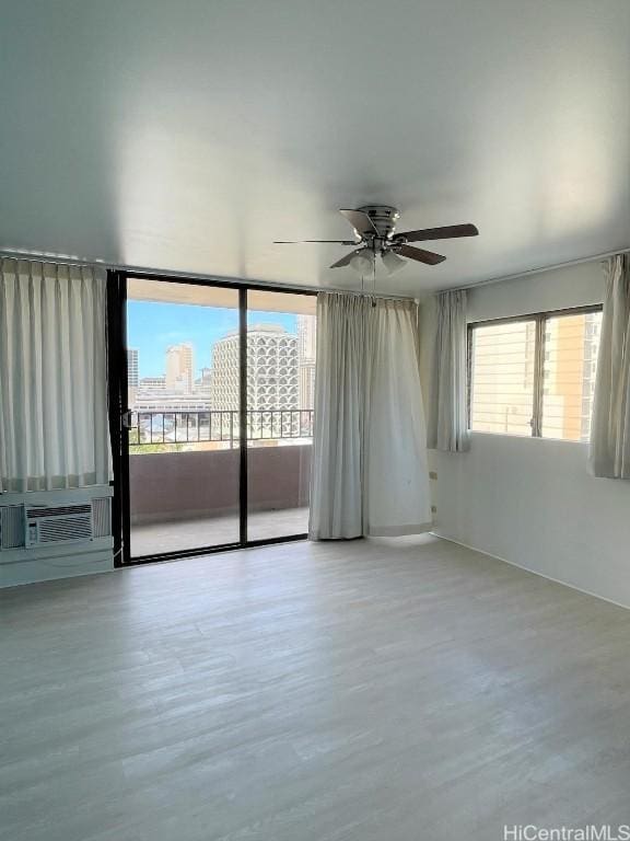 unfurnished room featuring a view of city, cooling unit, ceiling fan, and light wood finished floors