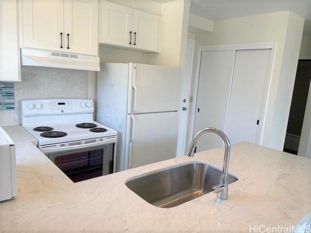 kitchen featuring white appliances, white cabinets, light stone countertops, under cabinet range hood, and a sink