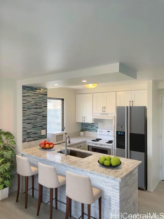 kitchen with a peninsula, white appliances, a breakfast bar, a sink, and white cabinets