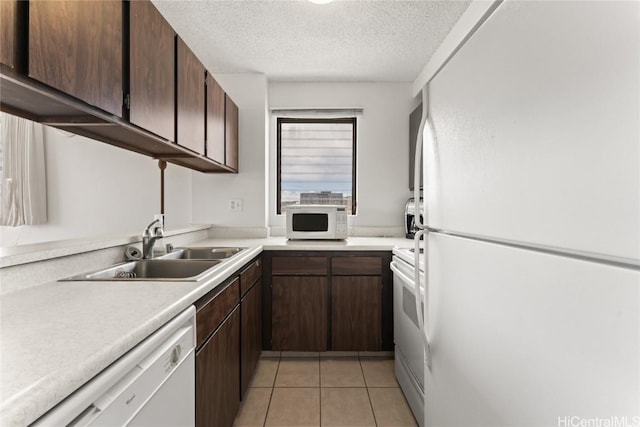 kitchen with white appliances, light tile patterned floors, dark brown cabinetry, a textured ceiling, and sink