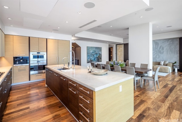 kitchen featuring sink, an island with sink, double oven, light stone counters, and dark hardwood / wood-style floors