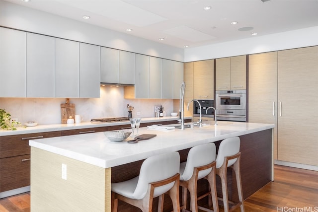 kitchen featuring wood-type flooring, appliances with stainless steel finishes, an island with sink, and a kitchen breakfast bar