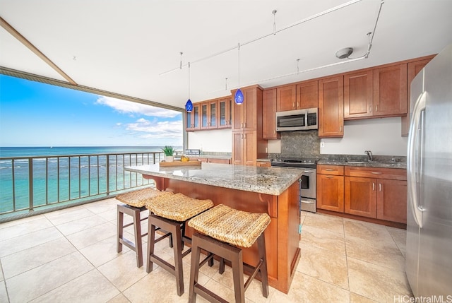 kitchen with a breakfast bar area, stainless steel appliances, a center island, light stone countertops, and a water view