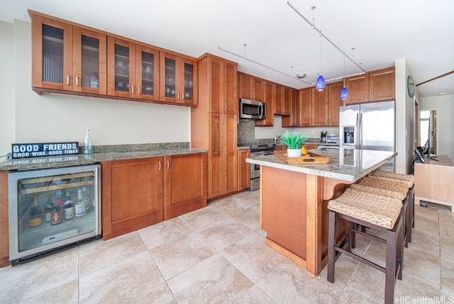 kitchen with stainless steel appliances, wine cooler, light stone countertops, a kitchen bar, and decorative light fixtures