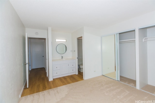 unfurnished bedroom with ensuite bathroom, multiple closets, sink, and light wood-type flooring