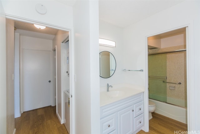 full bathroom with vanity, combined bath / shower with glass door, hardwood / wood-style flooring, and toilet