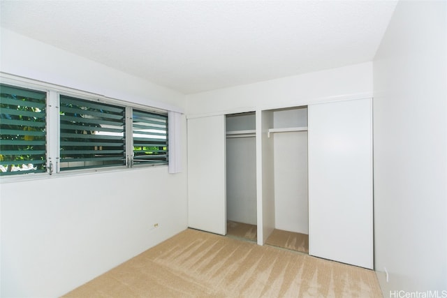 unfurnished bedroom with light carpet, a textured ceiling, and two closets