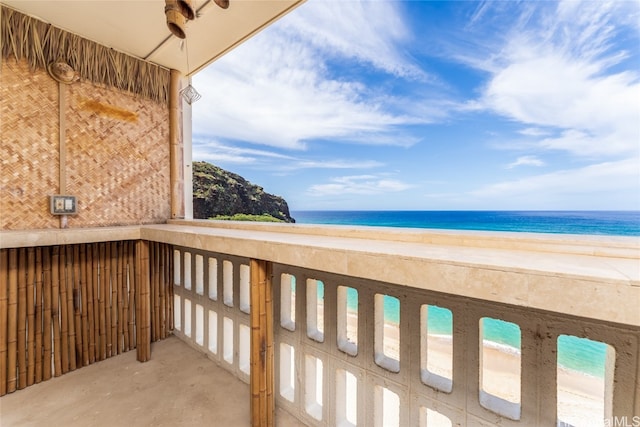 balcony with a view of the beach, a water view, and ceiling fan