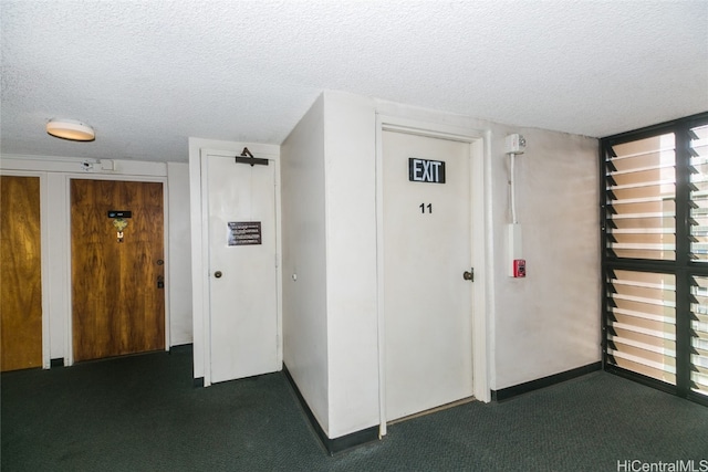 hallway featuring a textured ceiling and dark colored carpet