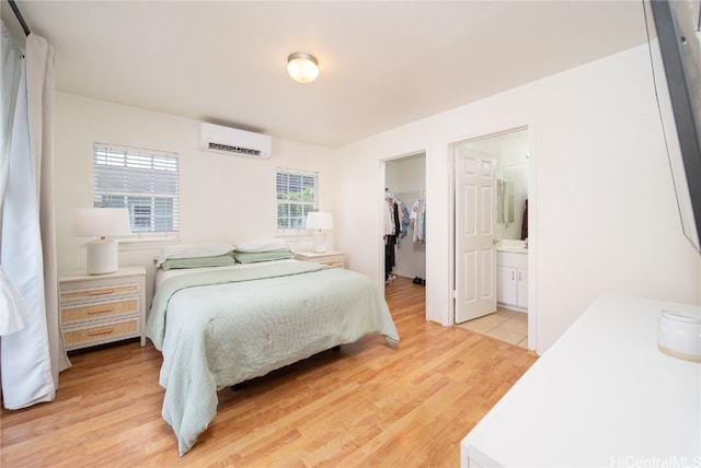 bedroom featuring a wall unit AC, a spacious closet, light hardwood / wood-style floors, a closet, and ensuite bath