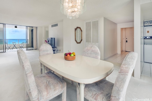 dining space with light tile patterned flooring, a chandelier, and stacked washer and clothes dryer