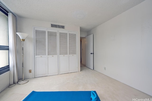 unfurnished bedroom with a textured ceiling, a closet, and light colored carpet