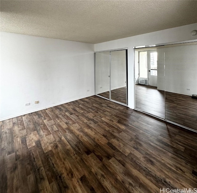 unfurnished bedroom with a textured ceiling, two closets, and dark hardwood / wood-style flooring