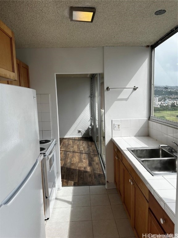 kitchen with tile countertops, light hardwood / wood-style flooring, electric stove, sink, and white refrigerator