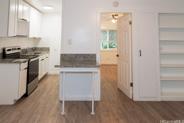 kitchen with sink, light wood-type flooring, stainless steel electric stove, white cabinets, and dark stone countertops