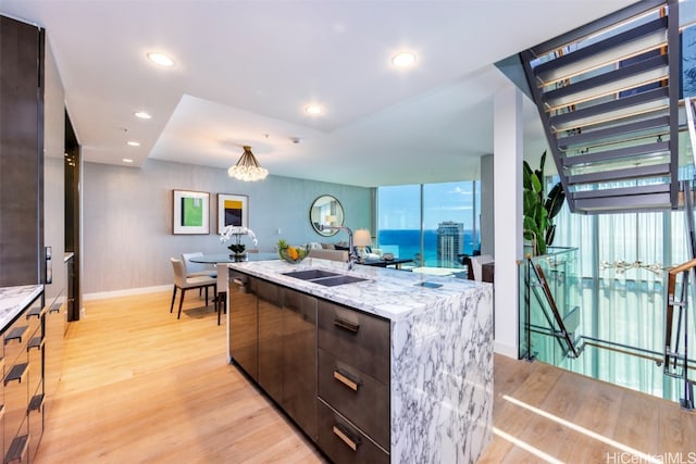 kitchen with dark brown cabinets, a center island with sink, light stone countertops, light wood-type flooring, and sink