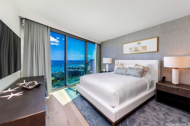 bedroom with a wall of windows, a water view, access to outside, and dark hardwood / wood-style flooring