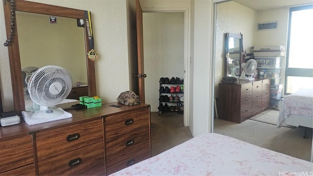 bedroom featuring a textured wall, visible vents, and light carpet