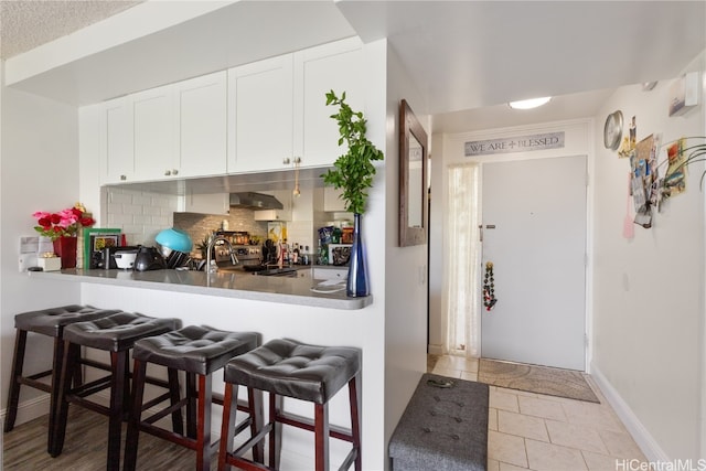 kitchen featuring extractor fan, decorative backsplash, white cabinets, and a breakfast bar area