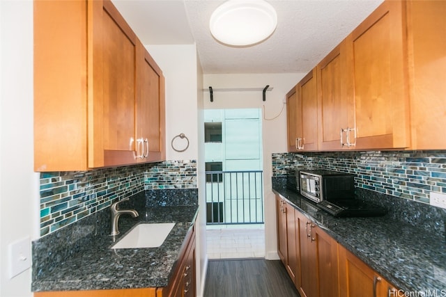 kitchen featuring sink, dark wood-type flooring, dark stone counters, and backsplash