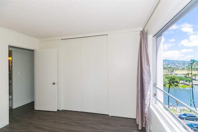 unfurnished bedroom with a water view, a textured ceiling, multiple windows, and dark hardwood / wood-style floors