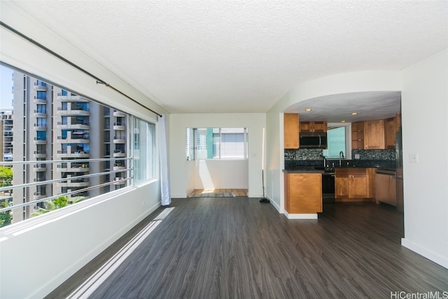 kitchen with dark wood-type flooring, a textured ceiling, stainless steel appliances, and backsplash