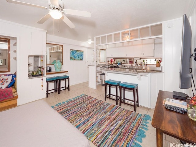 kitchen with light tile patterned floors, a breakfast bar area, ceiling fan, white cabinets, and kitchen peninsula