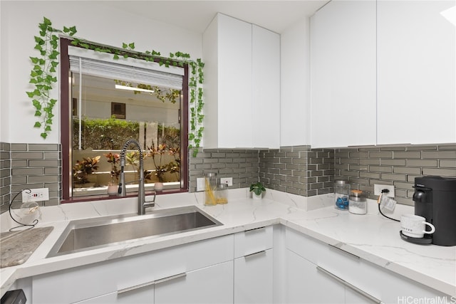 kitchen with white cabinetry, backsplash, sink, and light stone counters