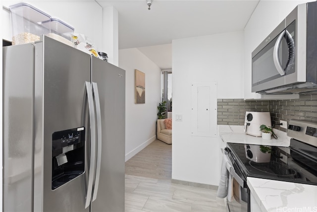 kitchen featuring light stone countertops, backsplash, white cabinetry, light hardwood / wood-style floors, and stainless steel appliances