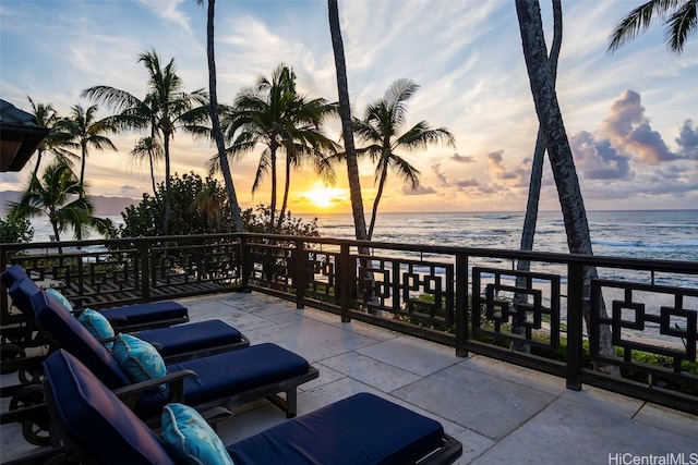 patio terrace at dusk featuring a balcony, a water view, and a view of the beach