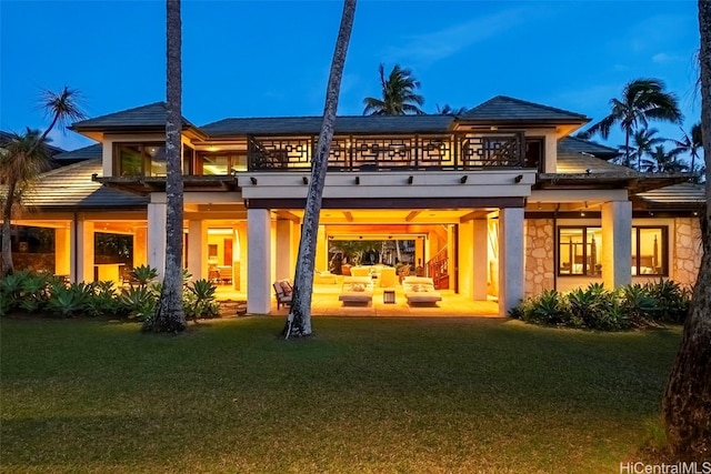 back house at dusk with a patio, outdoor lounge area, a yard, and a balcony