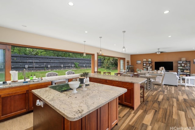 kitchen with a kitchen island, hardwood / wood-style floors, sink, light stone countertops, and decorative light fixtures