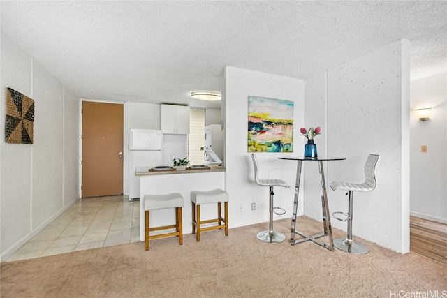 kitchen featuring light carpet, kitchen peninsula, white cabinets, a breakfast bar area, and white fridge