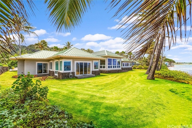 back of property with a water view, a lawn, and a sunroom