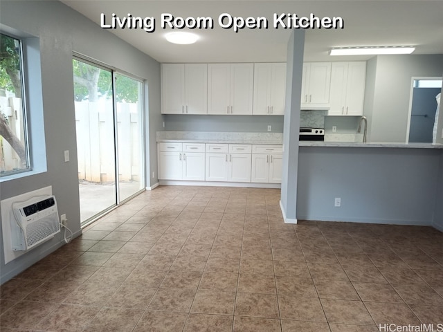 kitchen with sink, stainless steel range with electric cooktop, white cabinetry, light tile patterned floors, and a wall unit AC