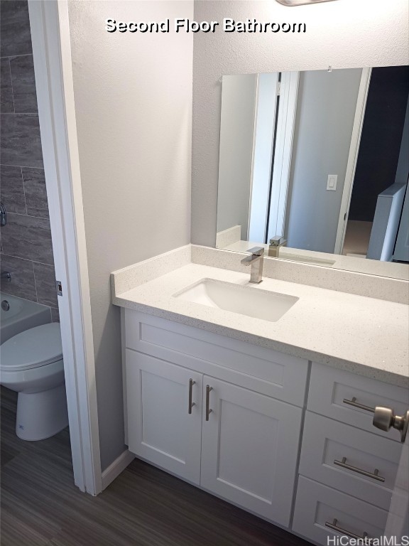 full bathroom with hardwood / wood-style flooring, vanity, tiled shower / bath, and toilet