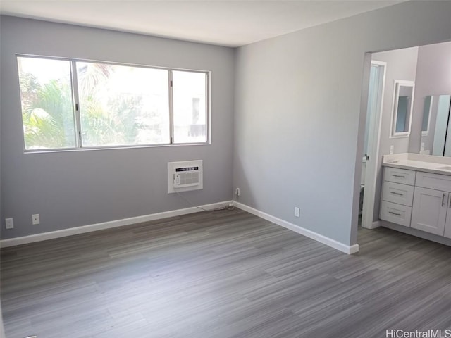 unfurnished bedroom with ensuite bath, a wall mounted air conditioner, and light hardwood / wood-style flooring