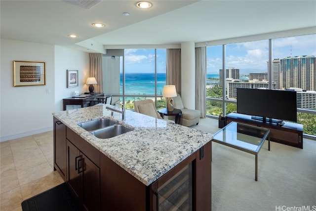 kitchen with beverage cooler, a center island with sink, sink, light tile patterned floors, and light stone counters