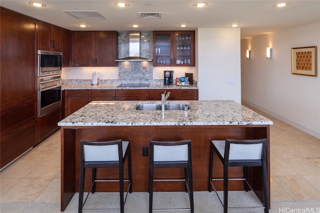 kitchen featuring wall chimney range hood, a breakfast bar area, stainless steel microwave, light stone countertops, and sink