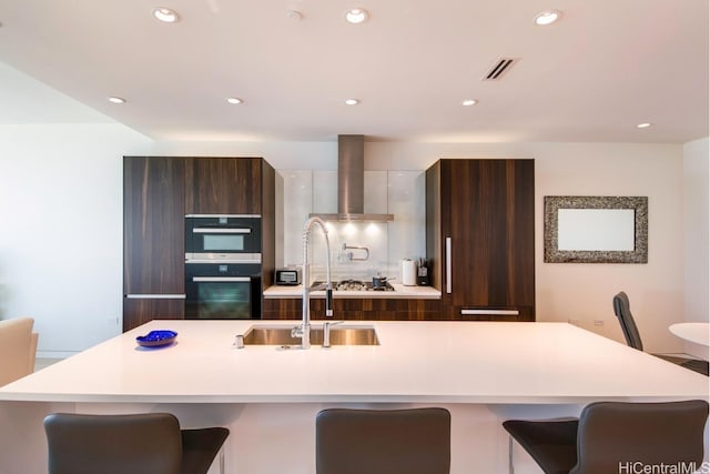 kitchen with a center island with sink, sink, a kitchen breakfast bar, and wall chimney exhaust hood