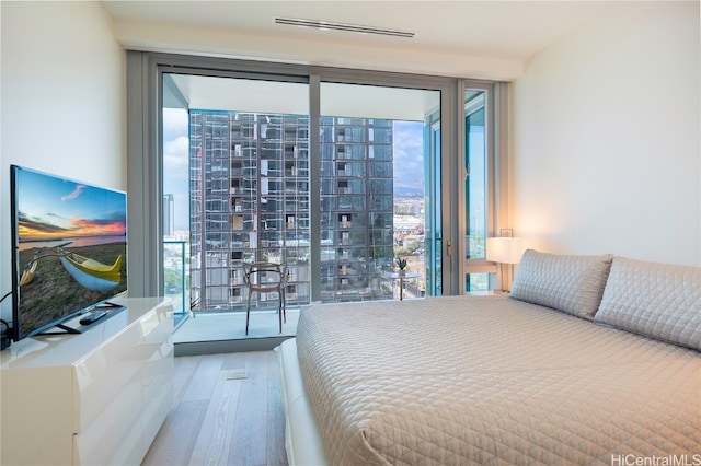 bedroom with expansive windows, multiple windows, access to outside, and wood-type flooring