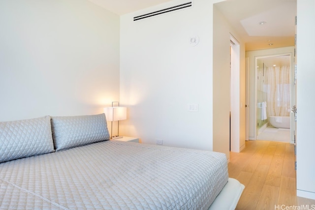 bedroom with a wall mounted AC, light wood-type flooring, and ensuite bath