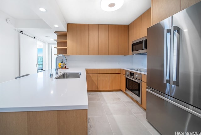 kitchen with kitchen peninsula, light tile patterned floors, appliances with stainless steel finishes, a barn door, and sink