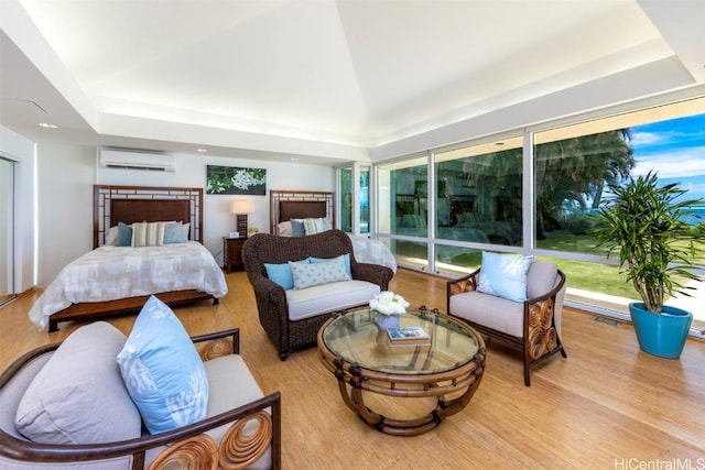 bedroom with lofted ceiling, a wall mounted AC, light hardwood / wood-style floors, and a tray ceiling