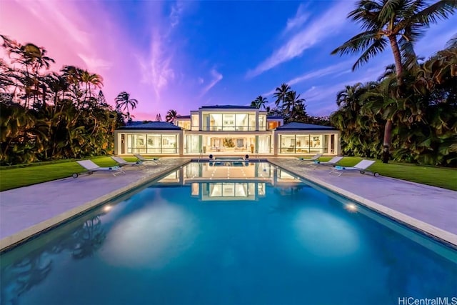 pool at dusk featuring a lawn and a patio area